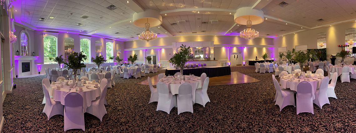 Banquet hall with white tables, large green foliage centerpieces, purple lighting and chandeliers