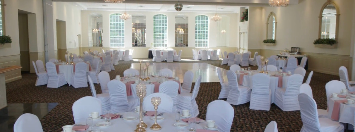 The Chateau Room features white table linens and pink napkins in ballroom with chandeliers and large windows